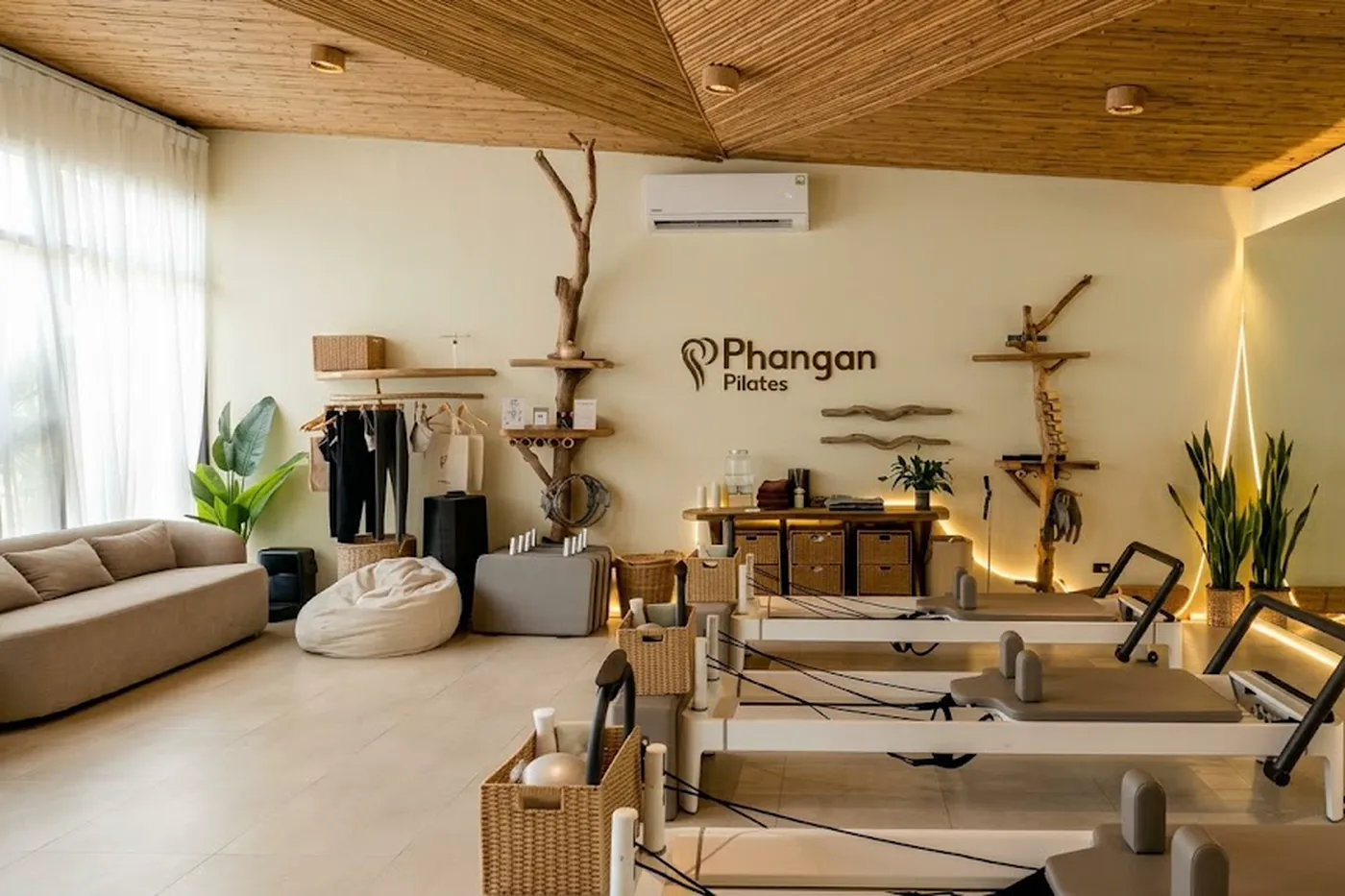 The studio's reception and lounge, with the Phangan Pilates wordmark on the wall and reformers lined up beyond a sofa and a rack of merchandise.
